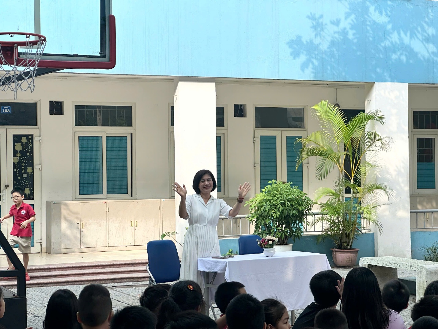 A person in a white dress standing on a table with a table with chairs and a basketball hoop

AI-generated content may be incorrect.