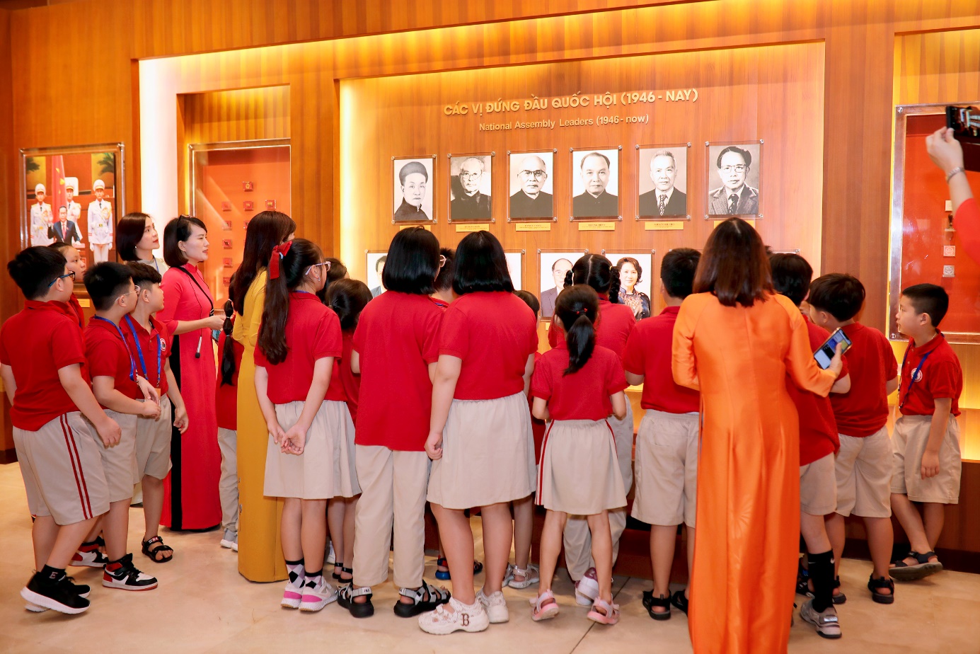 A group of people standing in front of a wall with pictures

Description automatically generated
