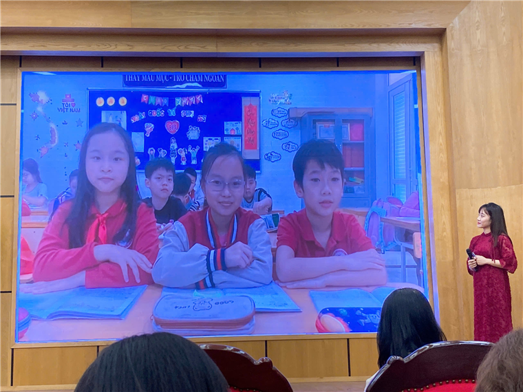 A group of children sitting in front of a large screen

Description automatically generated